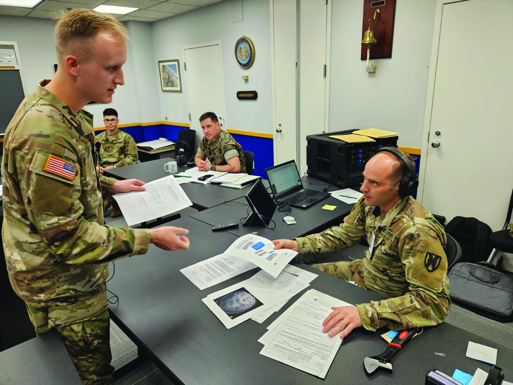 1LT Ethan Savage (standing, left), student in the 223d Officer Basic Course, hands exhibits to SSG Robert Zupa (seated, right), student in the 76th Basic Court Report Course, while participating in the U.S. v. Archer mock trial. The event included a mock guilty plea, military providence inquiry, and contested court-martial. (Credit: SSG Catherine Taylor)